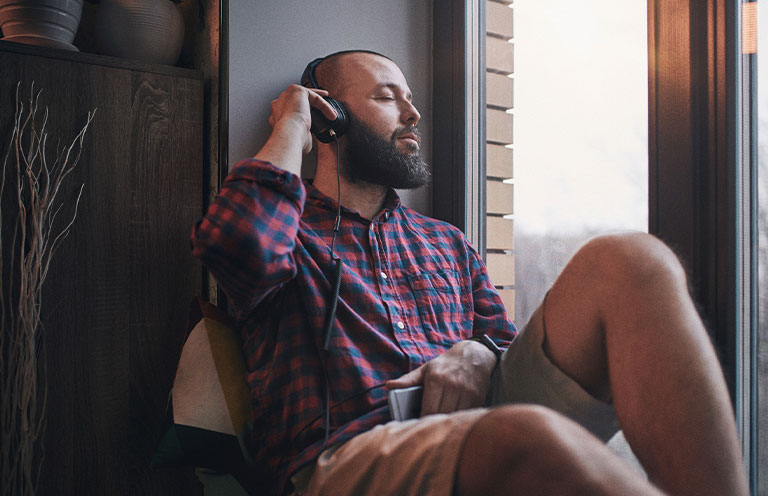 man sitting on window sill listening to music on headphones