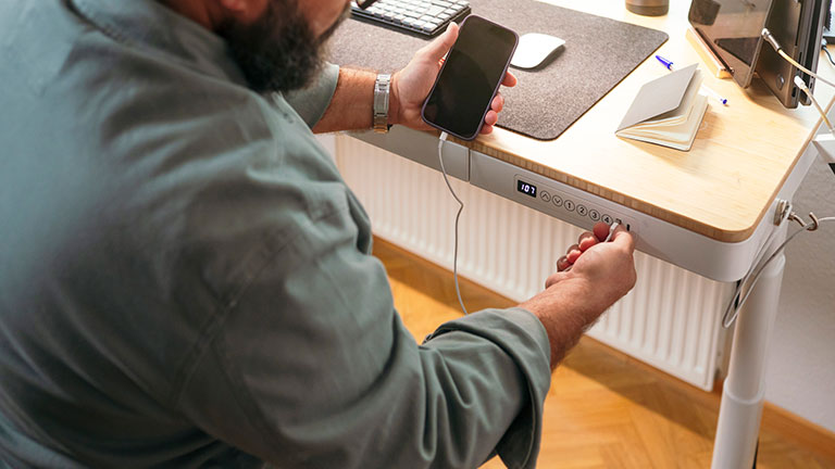 Man charging smartphone on electric standing desk