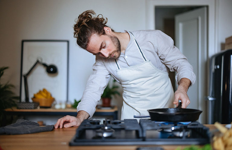 man turning on stove with cast iron skillet on burner