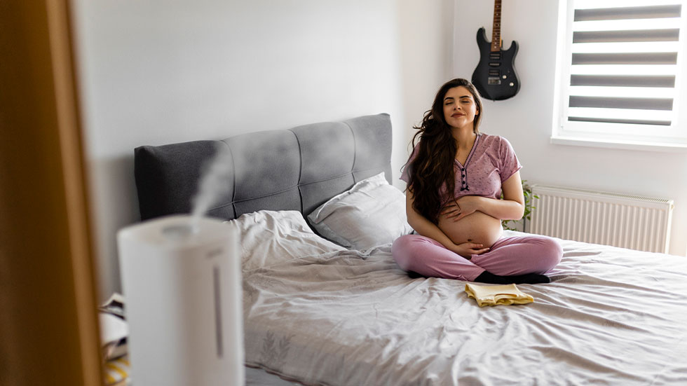 pregnant woman sitting on bed with air purifier on