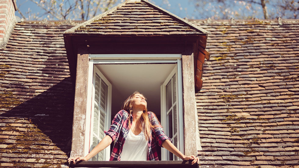 woman standing by open window inside of house