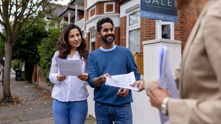 Real estate agent handling the blueprints of a house for sale to an Indian couple on the street and smiling Credit: andresr