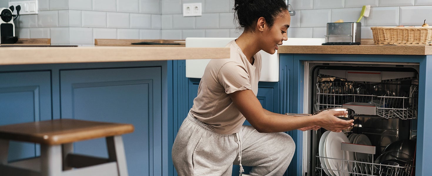 Happy black woman smiling while using dishwasher at home kitchen; by Drobot Dean
