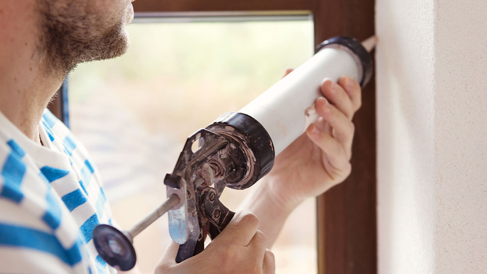 man using caulk gun on window