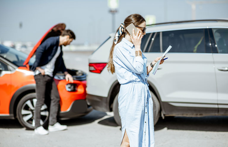 woman on phone, car accident scene behind her