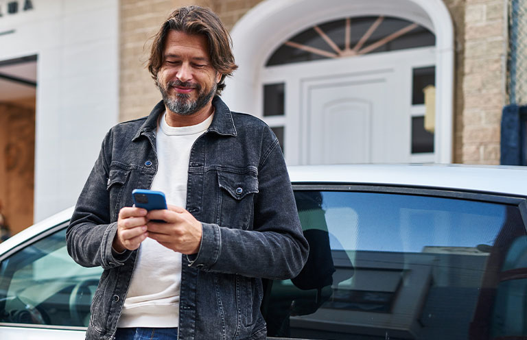 man using cell phone while standing outside of car