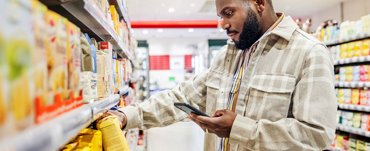 A man using his smartphone to look up ingredients and prices wile choosing items in his local supermarkets. Credit:TommL