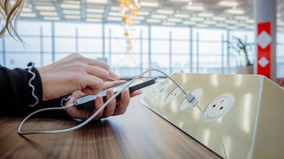 Close-up of a woman using her phone while charging it on a charging station in an airport terminal