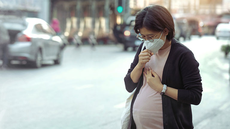 Asian pregnant woman wearing PM2.5 dust mask and coughing on the street. wearing mask protect against pollution, anti smog and viruses, air pollution, and headache suffocating. City air pollution. Credit:pcess609