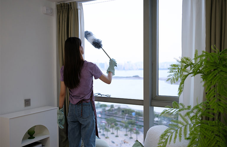woman cleaning window with dust wand