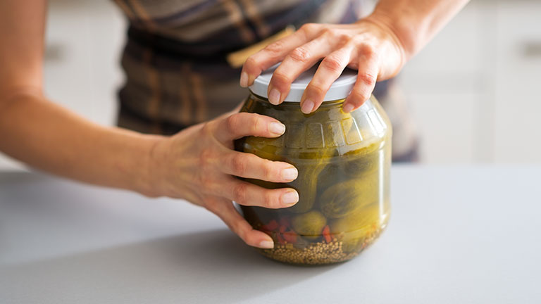 Closeup on young housewife opening jar of pickled cucumbers By Alliance