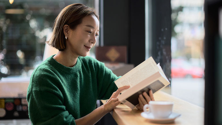 A young woman of Korean origin sits in the library by the window and reads a book while a cup of coffee stands next to her   Credit:Fotkam 