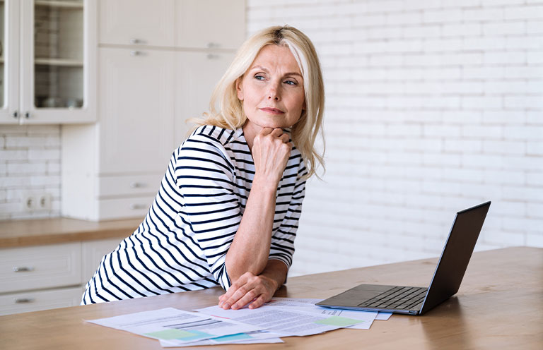 woman leaning on kitchen counter, laptop and papers on counter