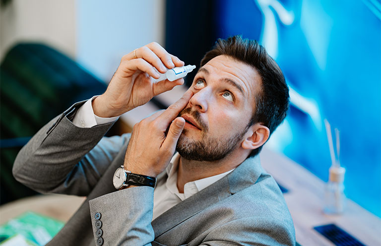 man applying eye drops to his eyes