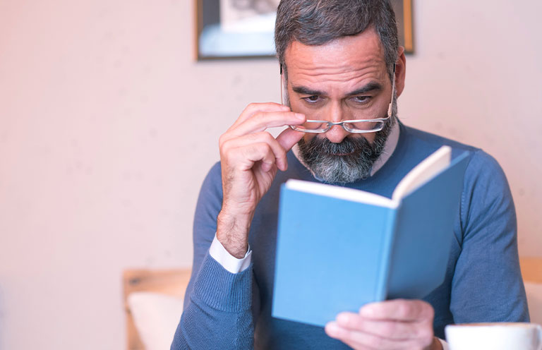 man adjusting glasses while holding book