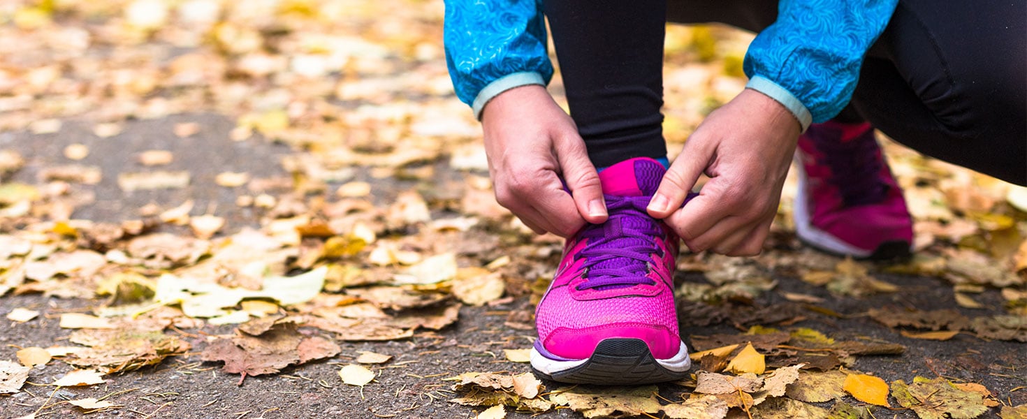 woman tying shoes, autumn leaves on ground