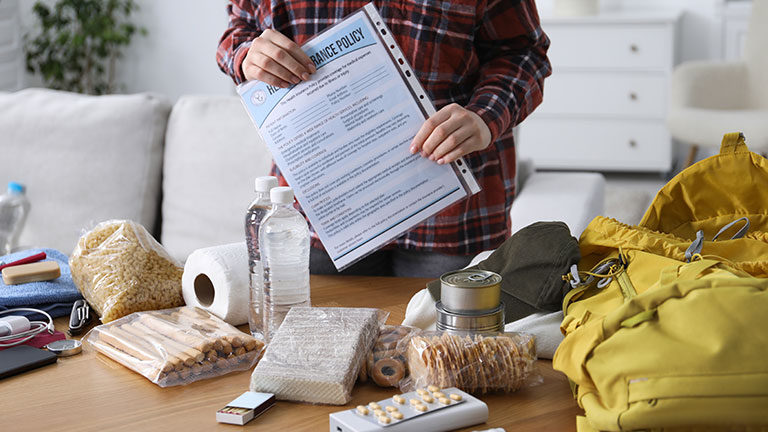 Survival kit. Woman holding documents near table with different emergency supplies indoors, closeup By New Africa