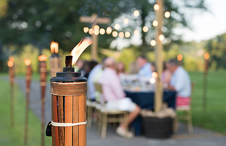 Tiki torch lit, people eating at table in background 