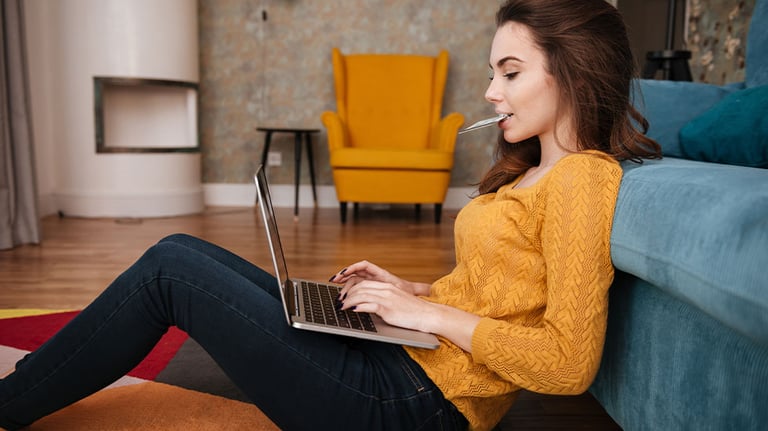 woman holding credit card between lips, using laptop