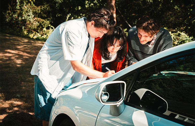 three friend gathered around the hood of a car