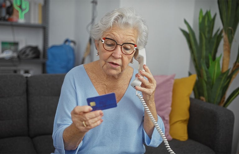 woman on phone holding and reading credit card