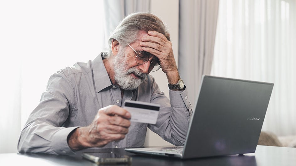 man holding head in hand while looking at laptop and credit card