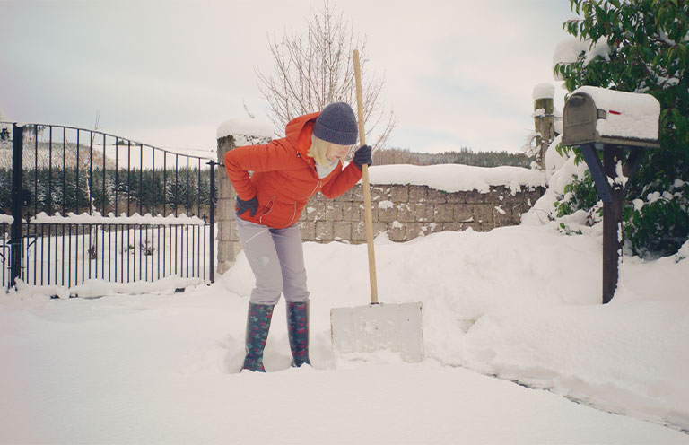 woman holding back in pain while shoveling snow