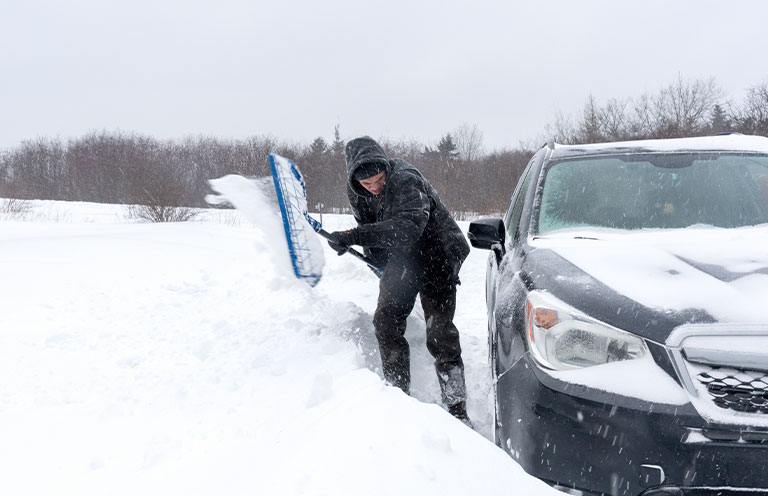 man shoveling snow around car