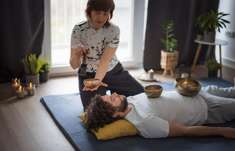 man in sound therapy session with sound bowls