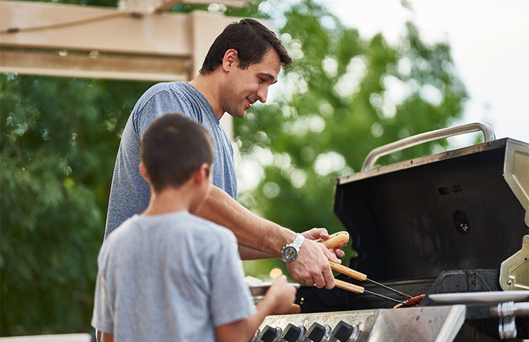 man putting hot dog from grill onto bun, little boy waiting
