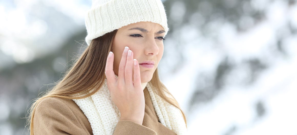woman with a painful expression outside in winter touching her face