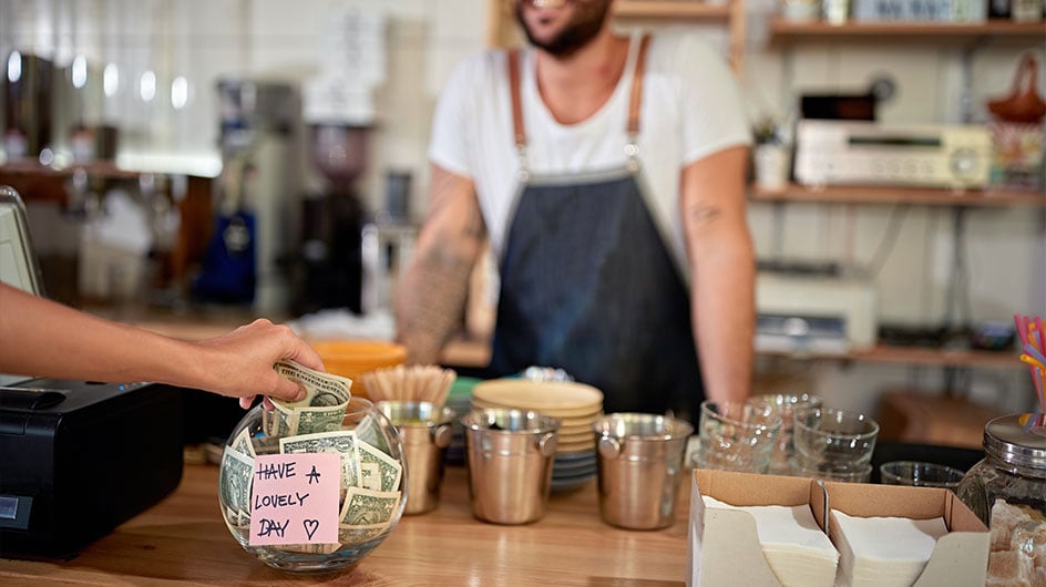 person putting money in a tip jar