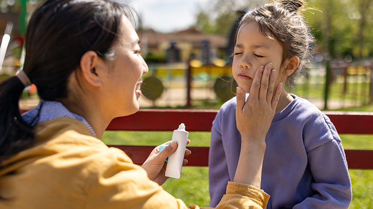 Mid adult Japanese woman applying sun-screen to her daughters face; Credit: miodrag ignjatovic