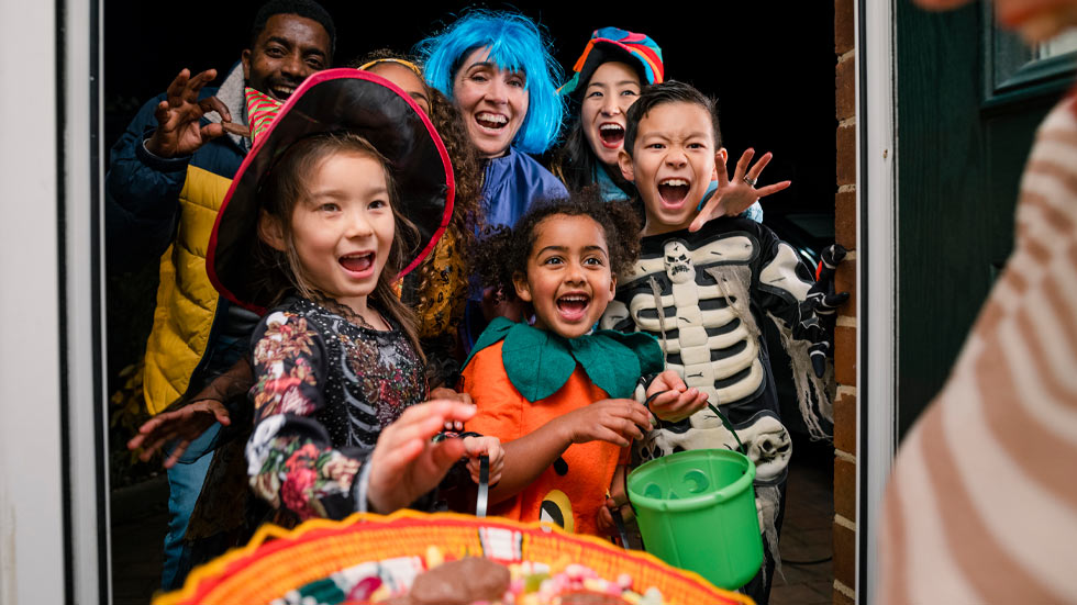 Children dressed in Halloween costumes in doorway getting candy