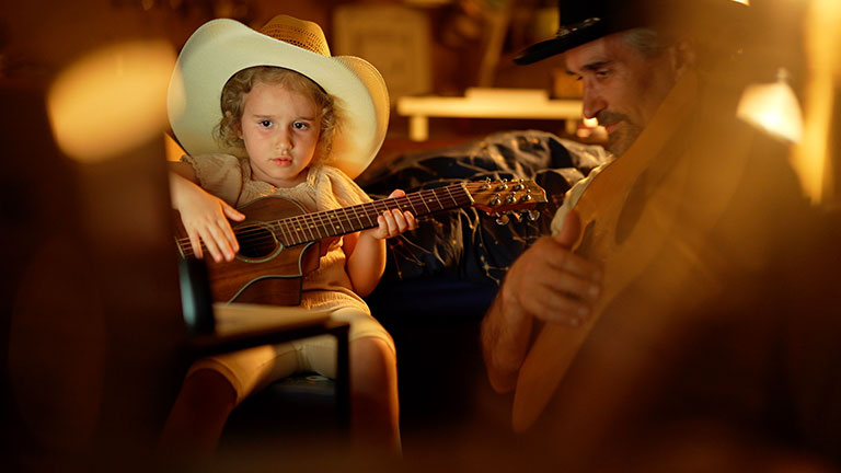 Family moments at night. Father & little daughter have fun playing country music duo on guitar illuminated by soft electric light & laptop. Love & sharing time. Credit:Daniel Balakov