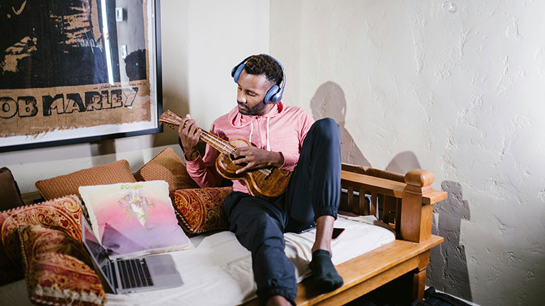 A Man Sitting on a Wooden Sofa while Playing Ukulele Credit: RDNE Stock project