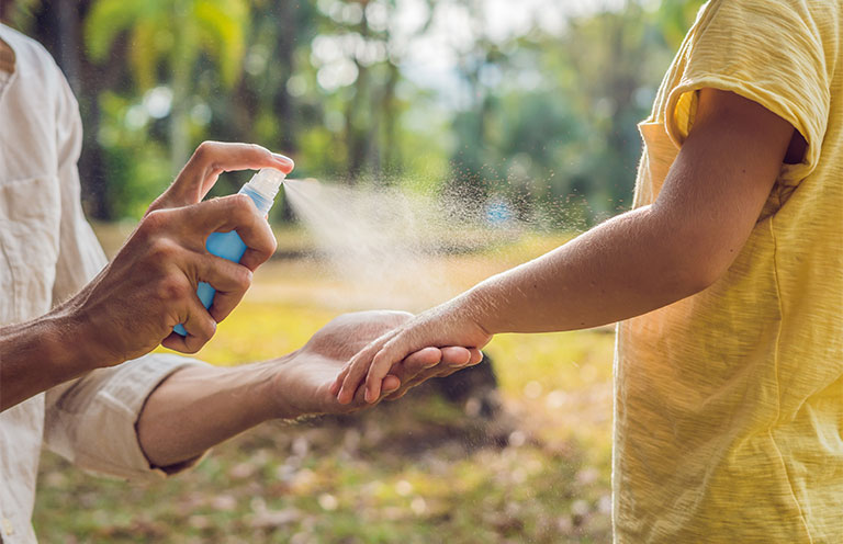 woman spraying mosquito repellant on child's arm