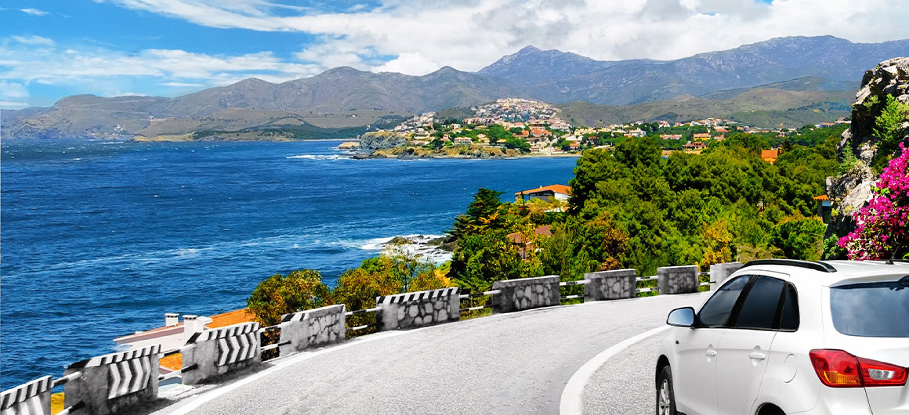 A white car drives by the road in mountains to the sea