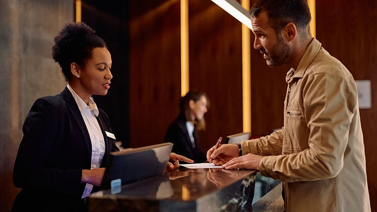 African American female receptionist assisting a guest with filling out documents while checking in at the hotel. Credit: Drazen Zigic