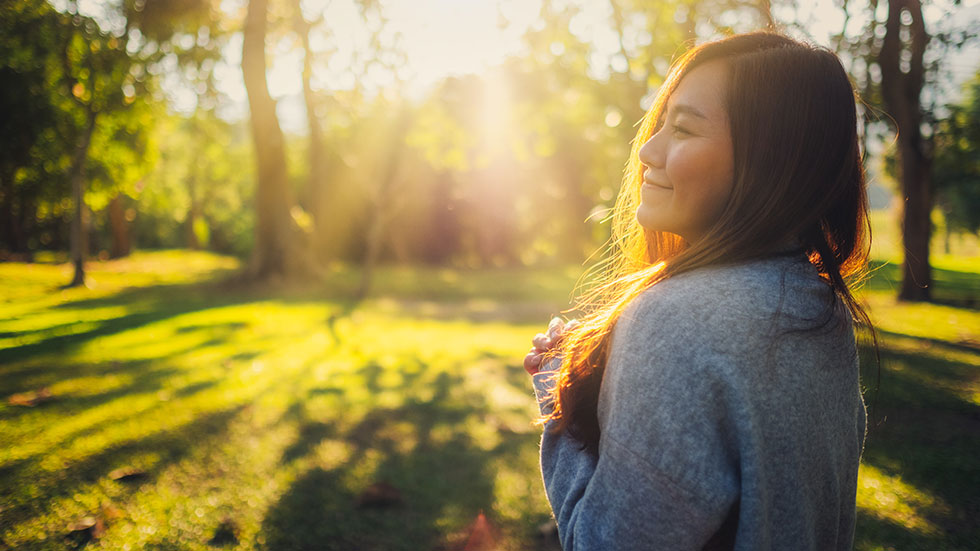 Asian woman standing among nature in a park before sunset.