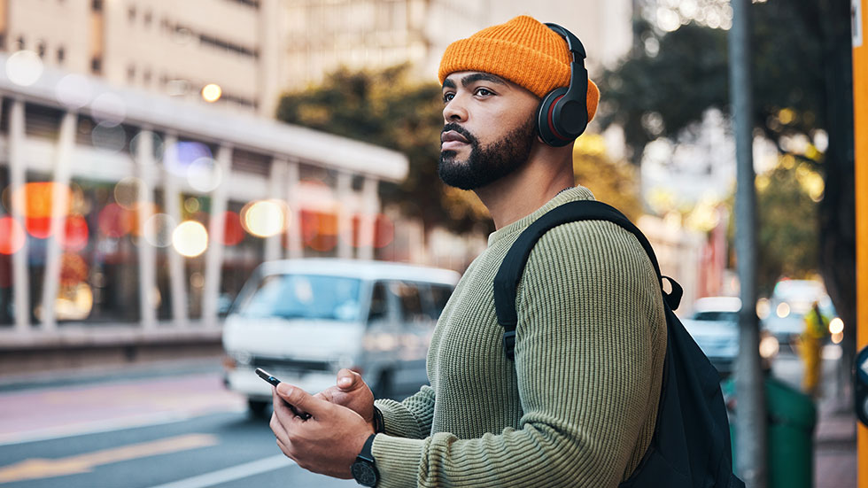 Man in street using phone and headphones to stream music or podcasts.