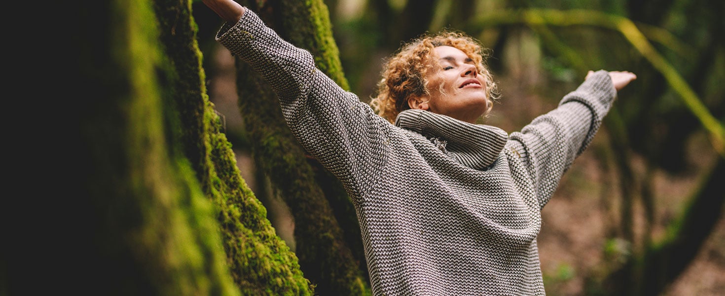 Overjoyed happy woman enjoying the green beautiful nature woods forest around her - concept of female people and healthy natural lifestyle - happiness emotion and adult lady opening arms close eyes. By simona