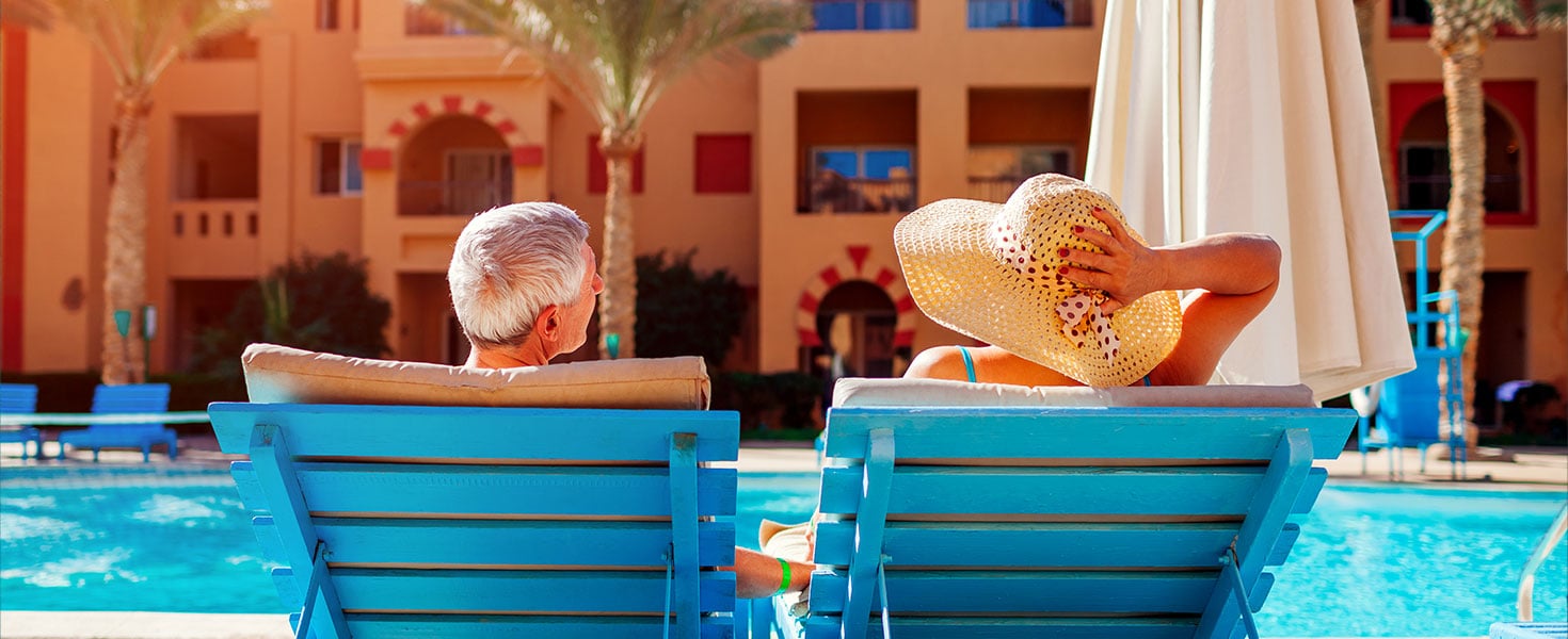 Senior couple relaxing by swimming pool lying on chaise-longues. People enjoying summer vacation. By maryviolet