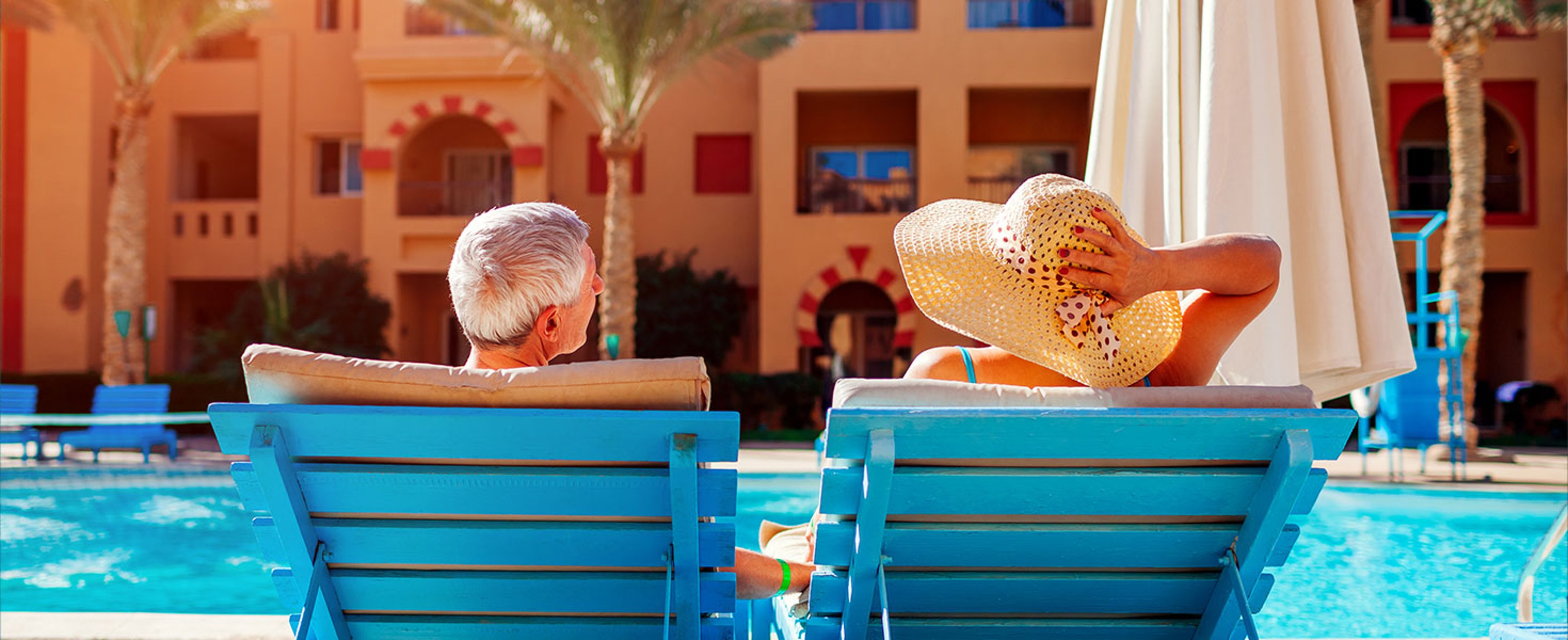 Senior couple relaxing by swimming pool lying on chaise-longues. People enjoying summer vacation. By maryviolet