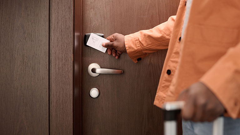 Close up of guest opening hotel room door and pressing keycard to NFC security lock system copy space By Mediaphotos