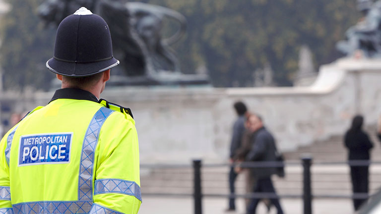 A British police man stands on duty across the road from Buckingham Palace, as tourists pass by in the background on their way to see the Changing of the Guard. Credit:RFStock