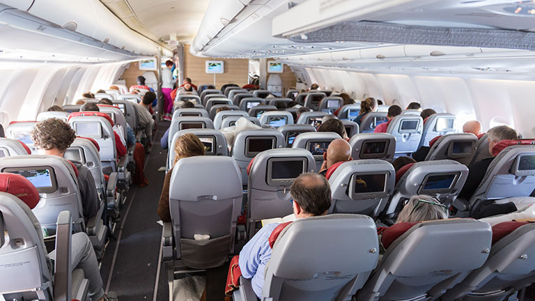 Interior of large commercial airplane with unrecognizable passengers on their seats during flight. By kasto