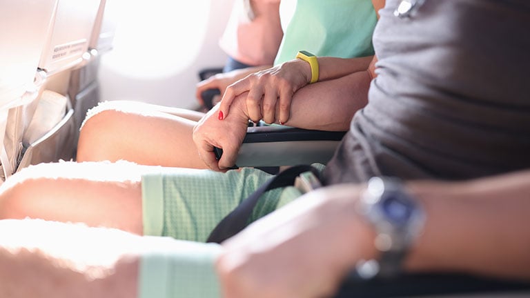 Woman firmly holds man's hand during flight in plane. Aerophobia of altitude concept. By H_Ko
