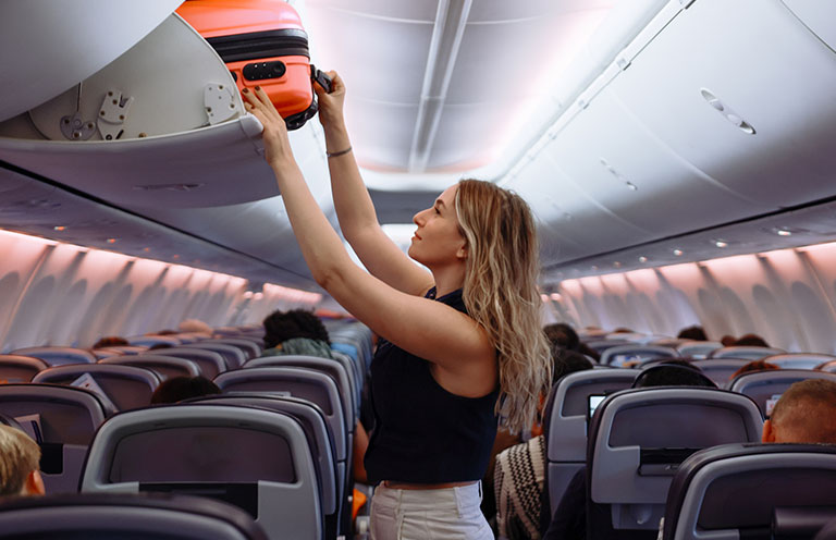 woman storing suitcase in overhead compartment on plane