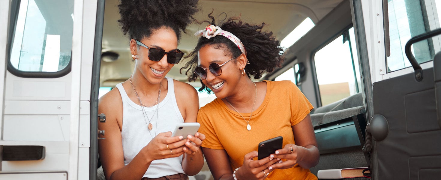 Two women sitting in RV smiling at smartphones
